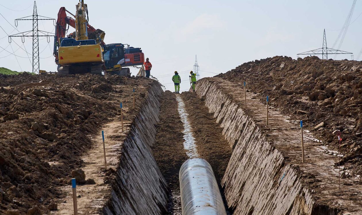 Eine große Pipeline-Baustelle. Arbeiter und Maschinen verlegen unterirdische Leitungen für die künftige Gas- und Wasserstoffversorgung quer durch landwirtschaftliche Flächen.