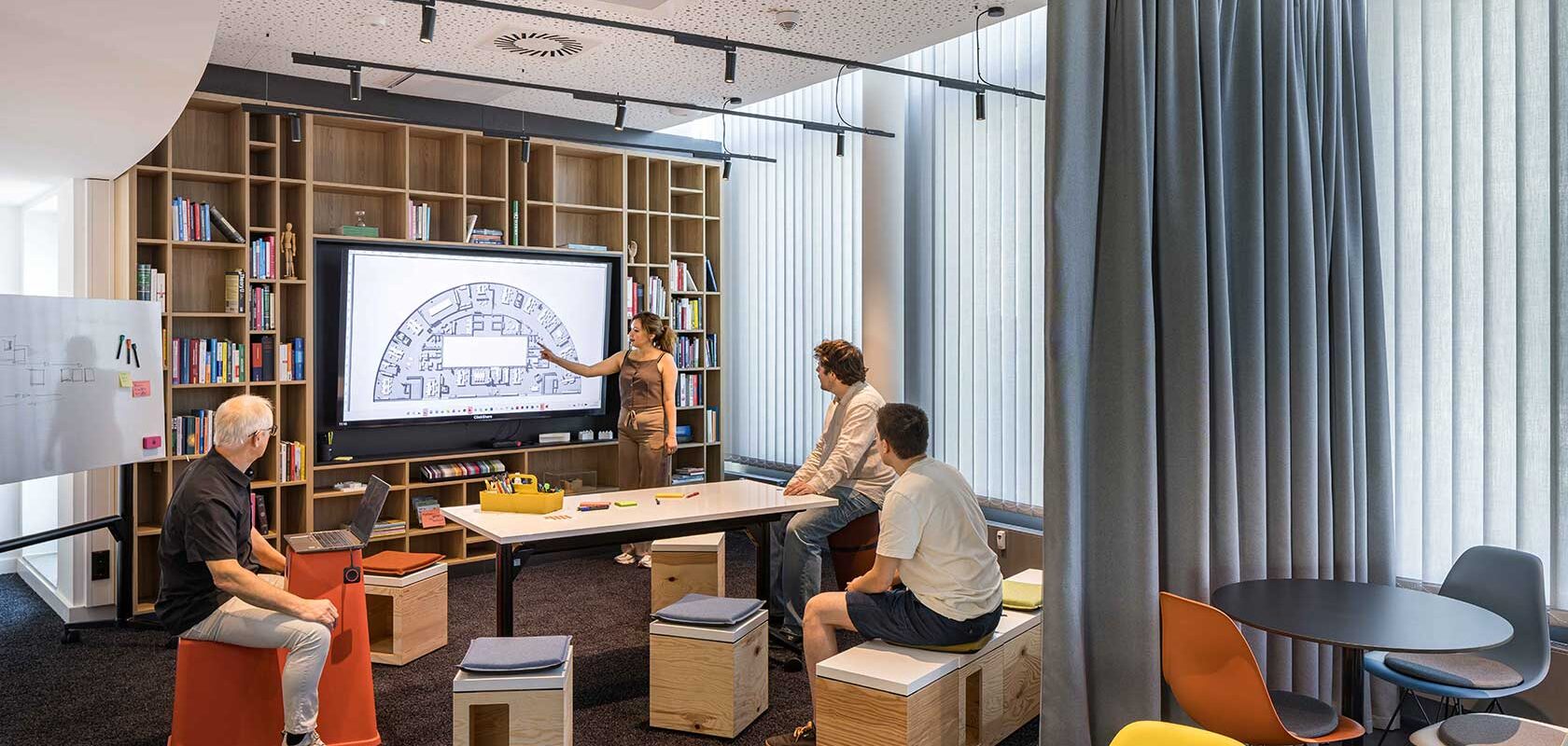 Meetingraum, Sweco Köln – Bildschirm mit Grundrissplan, Plywood-Hocker und Vorhang in Orange