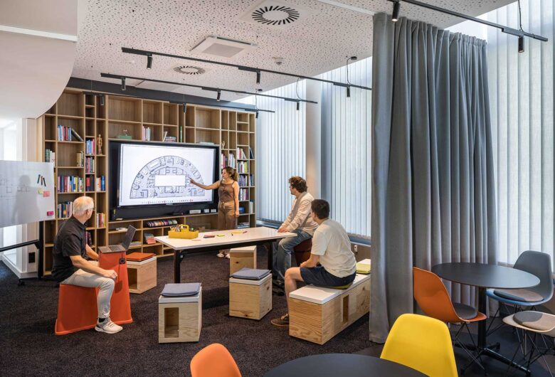 Meetingraum, Sweco Köln – Bildschirm mit Grundrissplan, Plywood-Hocker und Vorhang in Orange